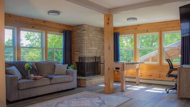 A cozy living room with a stone fireplace, a sofa, and a coffee table. - The Crossmon House (Alexandria Bay)