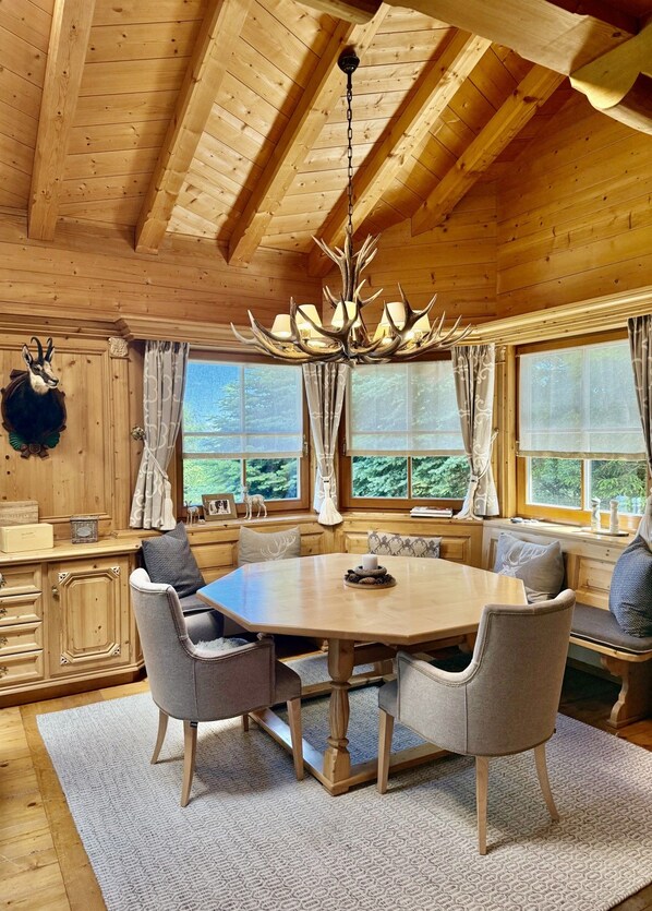 A wooden interior with a round table, chairs, and a chandelier.