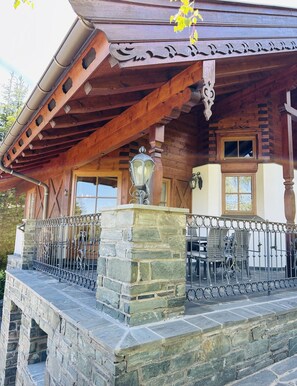 A wooden cabin with a stone foundation, a balcony with metal railings, and a window with a view.