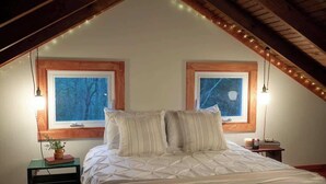 Un dormitorio con una cama grande, dos ventanas y luces colgantes.