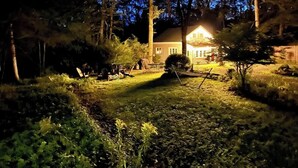 Una casa con un jardín delantero bien iluminado de noche, rodeada de árboles.