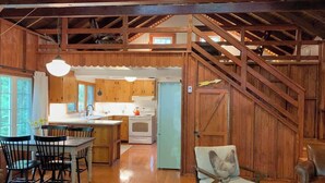 Interior rústico de una cabaña con comedor, cocina y una escalera que conduce a un nivel superior.