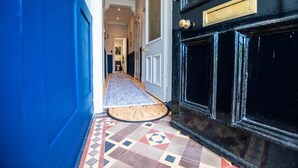 Un pasillo con piso estampado, pared azul y puerta negra con picaporte de latón.