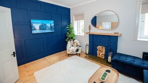 Una sala de estar con pared azul, puerta blanca, chimenea, sofá, televisor y planta.