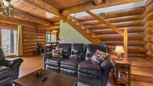 A log cabin interior with a leather sofa, wooden table, and a staircase. - Mountain View Log Cabin in the White Mountains (Dalton)