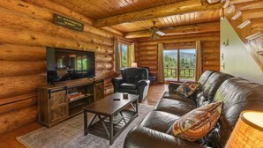 A log cabin interior with a television, leather sofa, and a sign indicating the location as Mt. Washington Summit. - Mountain View Log Cabin in the White Mountains (Dalton)