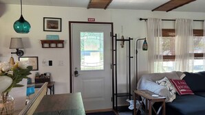 A cozy room with a door marked "EXIT," a window with blinds, a blue sofa with a pillow, and a small table with a vase of flowers. - Port Clinton Lakeside Escape (Erie Township)