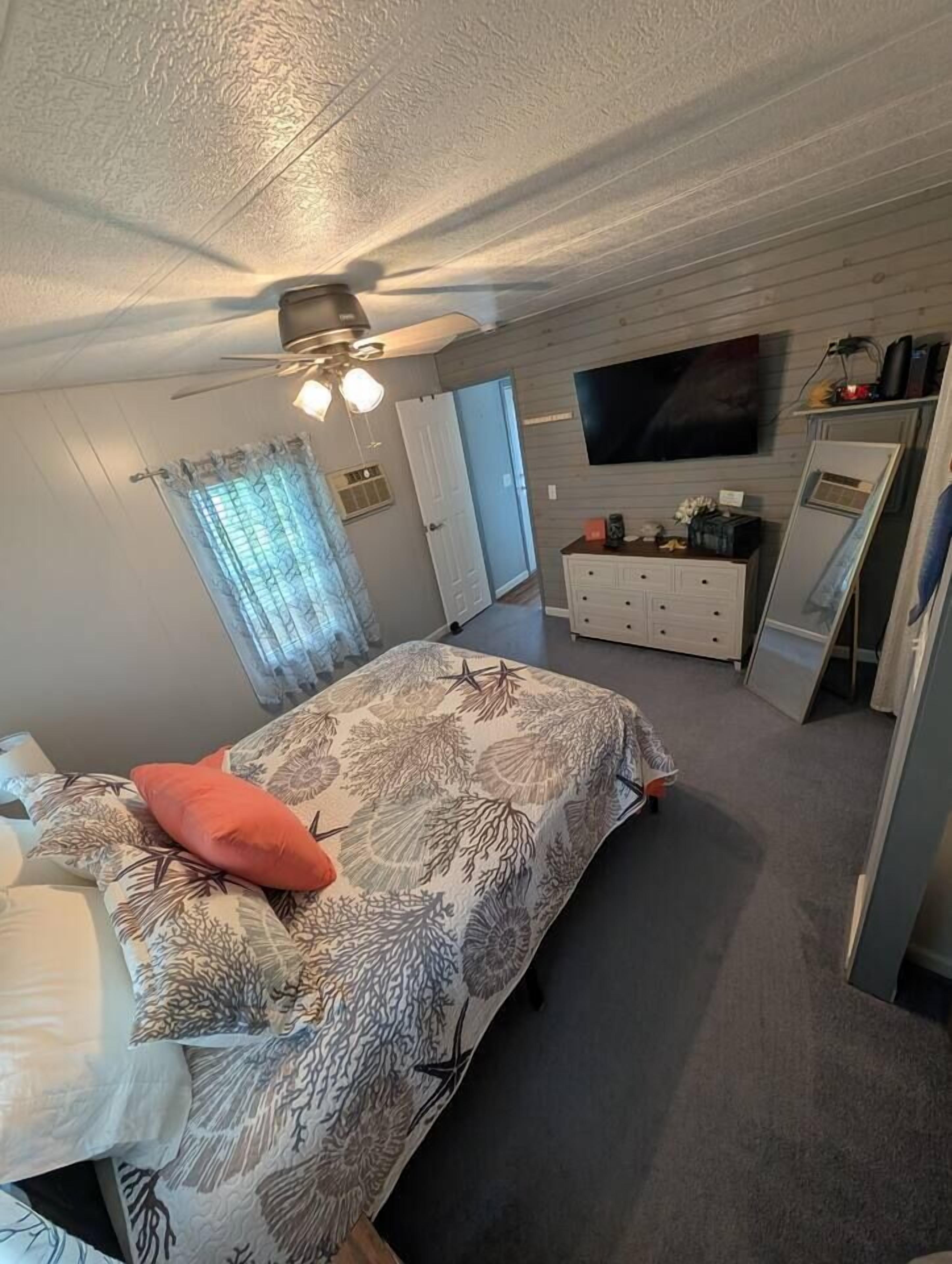 Een slaapkamer met een bed, een dressoir, een televisie en een spiegel.
