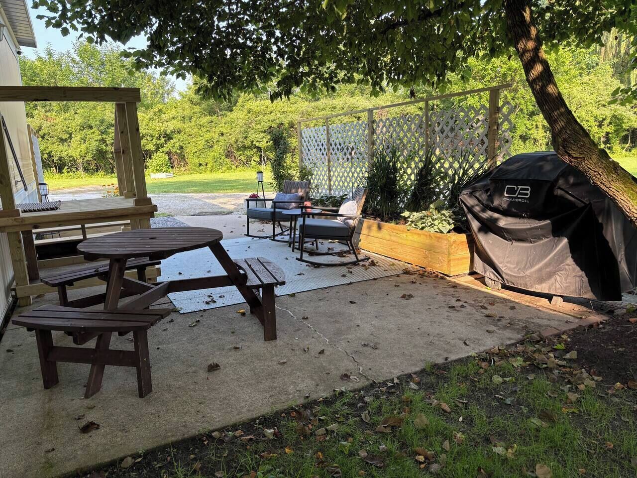 Een achtertuin met een houten tafel en stoelen, een barbecue en een overdekte zithoek.