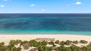 Een strand met helder turquoise water, een zandstrand en een rij rieten parasols.