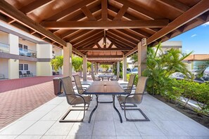 Een terras buiten met een overdekte zithoek, een tafel en stoelen.