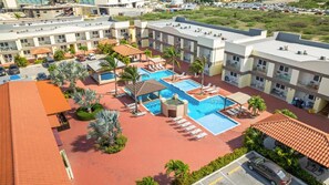 Un hôtel doté de plusieurs piscines, de palmiers et d’un bâtiment au toit rouge.