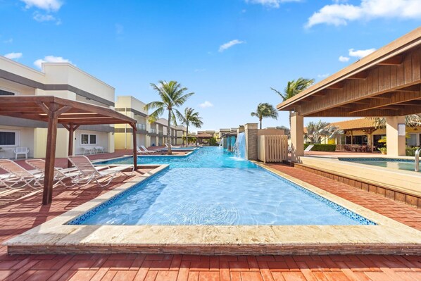 A pool area with lounge chairs, a water feature, and palm trees.
