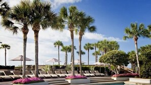 A pool area with lounge chairs and palm trees. - Luxury First Floor Villa - Free Daily Golf and Tennis Included (Hilton Head Island)