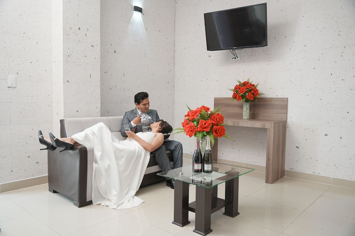 Quarto moderno com sofá, mesa de vidro com um vaso de flores e televisão de tela plana na parede.