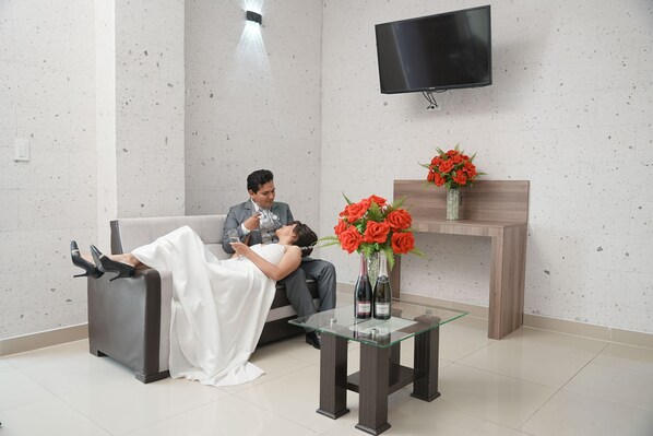 A modern room with a sofa, a glass table with a vase of flowers, and a flat-screen TV mounted on the wall.