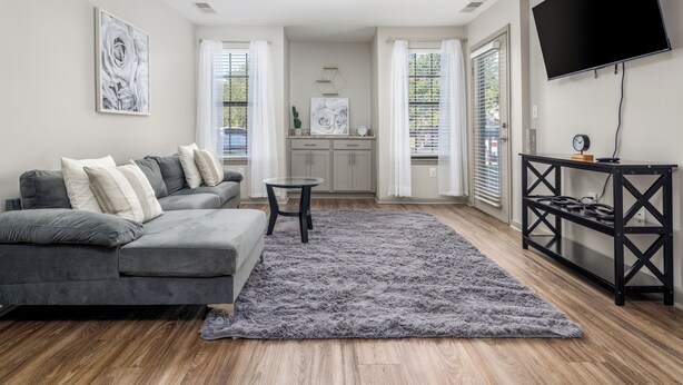 A modern living room with a grey sectional sofa, a glass coffee table, and a grey shag rug. - 3 mins from Space Center &BridgeStreet. (Huntsville)