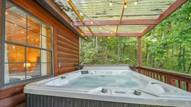 Un jacuzzi en una terraza de madera con un ventanal y una pérgola de madera encima.
