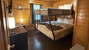 Una habitación de cabaña de madera con una cama litera, un escritorio con lámpara y una mesita de noche pequeña.