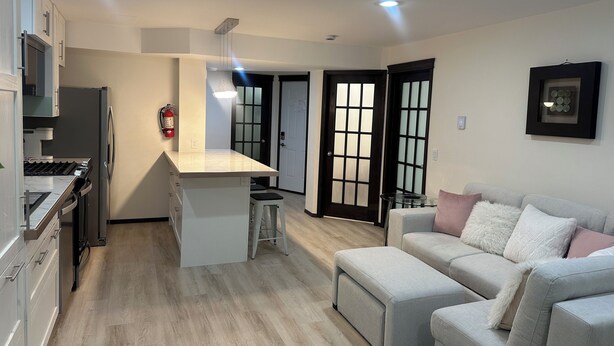 Eine moderne Küche mit Kochinsel, ein Essbereich mit Glastisch und ein Wohnzimmer mit Sofa und Hocker.
