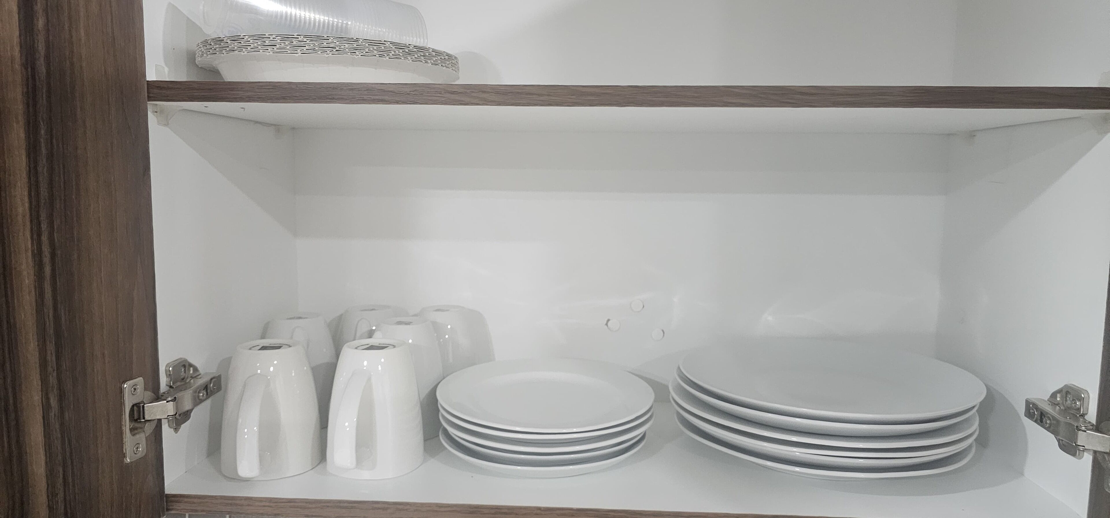 Een keukenkastje met witte borden, kommen en een waterkoker.