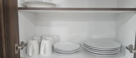 A kitchen cabinet with white plates, bowls, and a kettle.