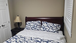 A bedroom with a bed, a nightstand with a lamp, a door, and a window with blinds.