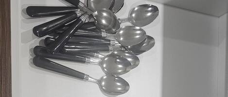 Une étagère blanche où sont rangés de manière ordonnée des couverts, notamment des cuillères, des fourchettes et des couteaux.