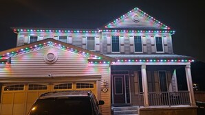A two-story house with a garage, adorned with colorful string lights.