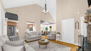 A spacious living room with a large grey sofa, a round coffee table, and a chandelier.