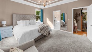 A bedroom with a large bed, a chandelier, a mirror, and a view of the outdoors.