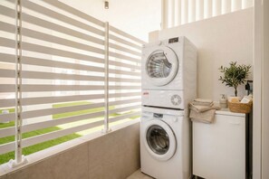A laundry area with a washing machine and dryer, a small plant, and a window with blinds. - Borgo Felice 5 (Cozy Apartment with Balcony) (Bari)