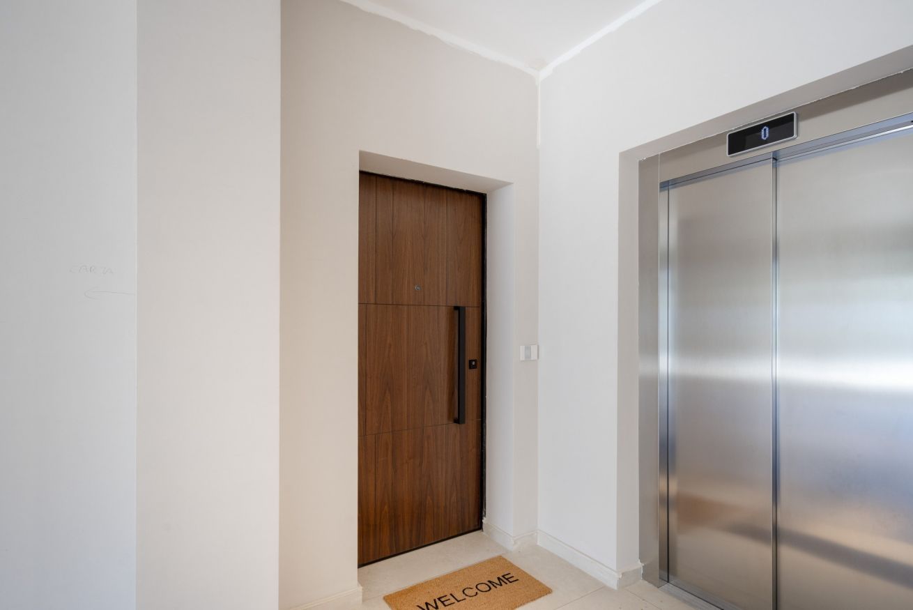 A modern elevator with a digital display, a wooden door, and a welcome mat.