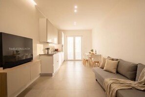 A modern apartment with a TV on a wooden stand, a kitchenette, a dining area, and a living room with a sofa. - Borgo Felice 5 (Cozy Apartment with Balcony) (Bari)