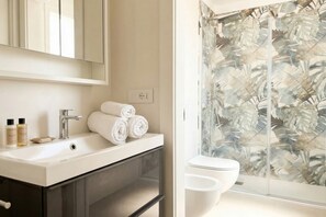 Een badkamer met een witte wastafel, een spiegel en een douche met een deur van glas met bladmotief.