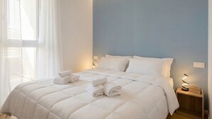 A neatly made bed with white bedding and rolled towels, a bedside lamp, and a window with sheer curtains. - Borgo Felice 5 (Cozy Apartment with Balcony) (Bari)