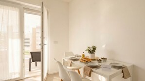 A dining area with a table set for two, a chair, a potted plant, and a sign with a website address. - Borgo Felice 5 (Cozy Apartment with Balcony) (Bari)