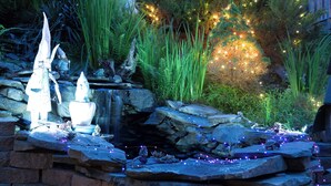 Ein Garten mit einem kleinen Wasserfall, dekorativer Beleuchtung und Steinbauten.