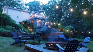 Ein Garten mit Feuerstelle, einer Holzterrasse und Gartenmöbeln.