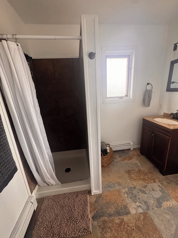 A bathroom with a shower, a sink, a window, and a towel rack.