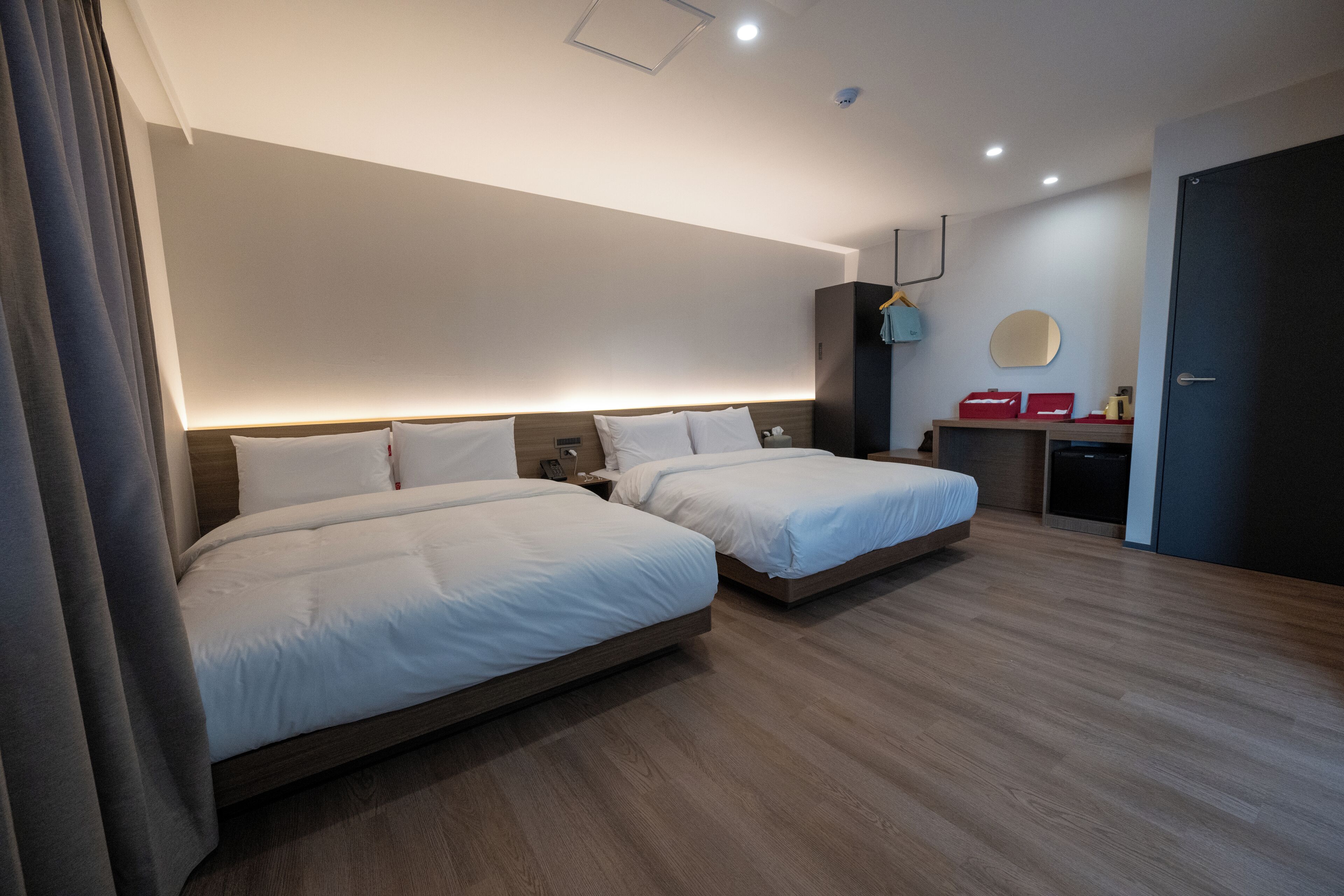 Una habitación de hotel moderna con dos camas, un escritorio, un espejo y un armario.