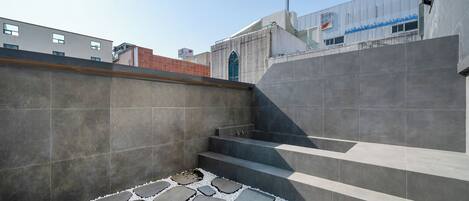 Un espacio exterior moderno con escalones de piedra y suelo de baldosas, rodeado de muros altos.