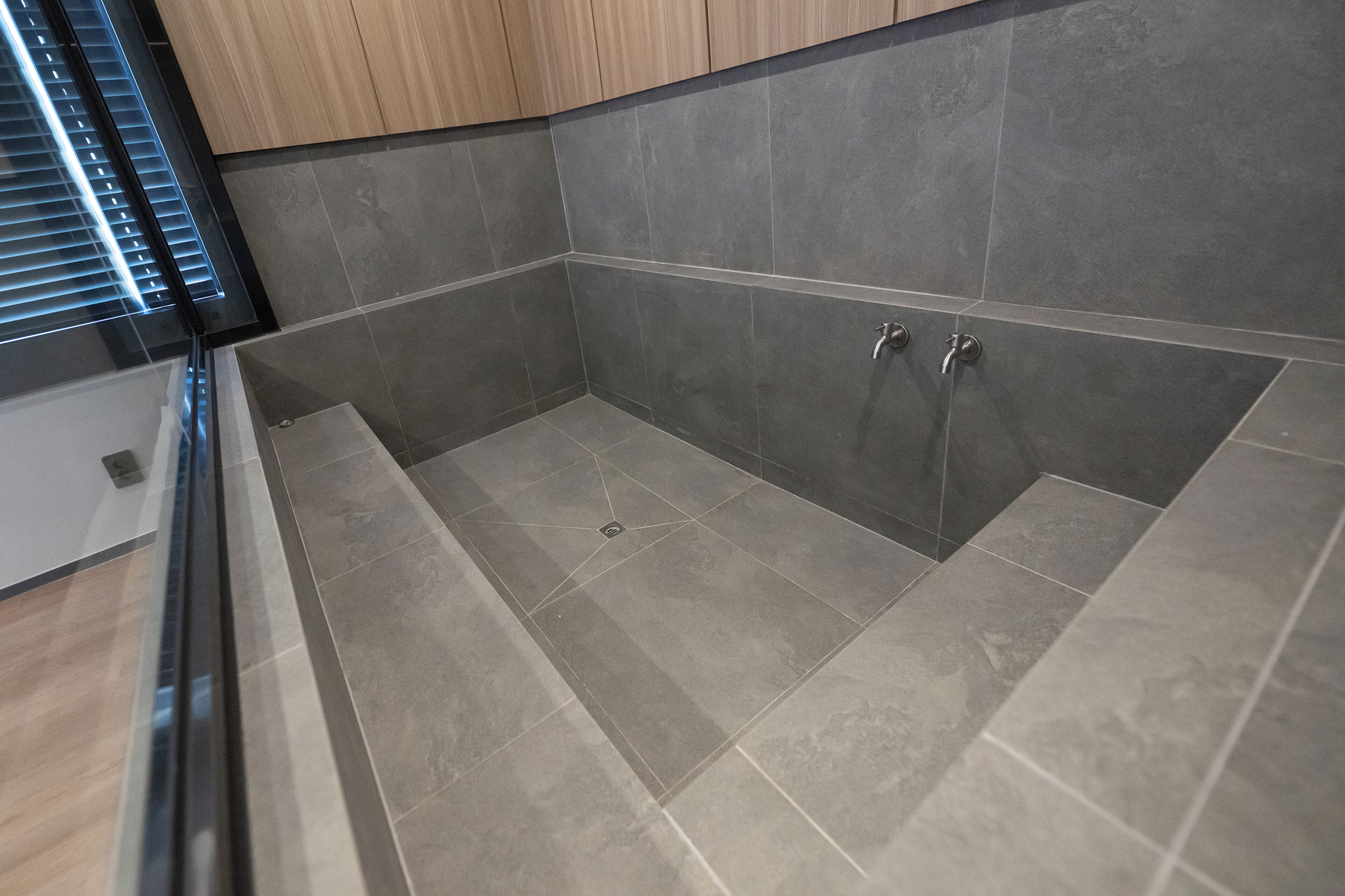 A modern bathroom with grey tiles, a glass shower enclosure, and wooden cabinets.