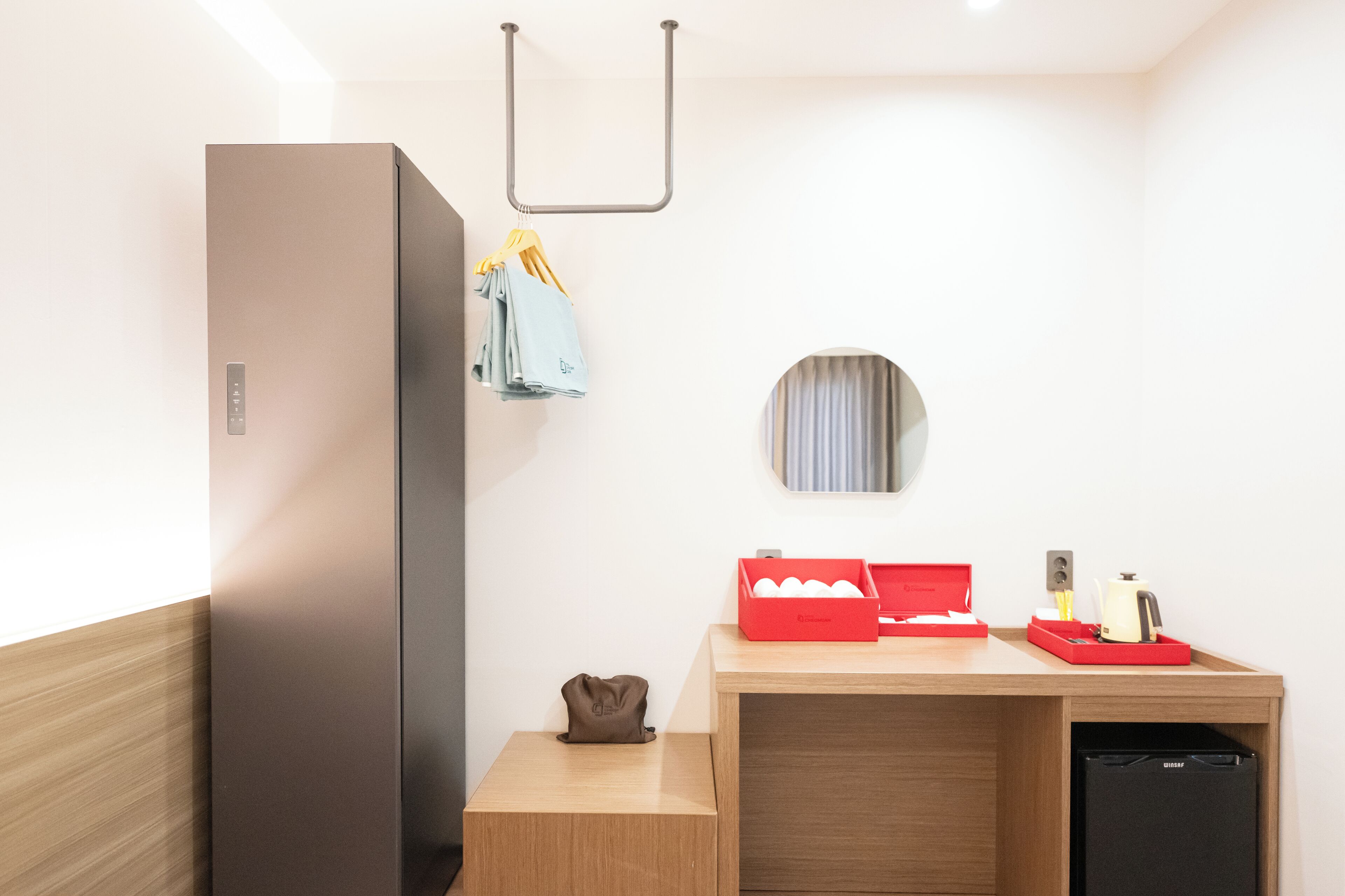 A compact kitchenette with a refrigerator, a sink, and a countertop with a red box and a kettle.