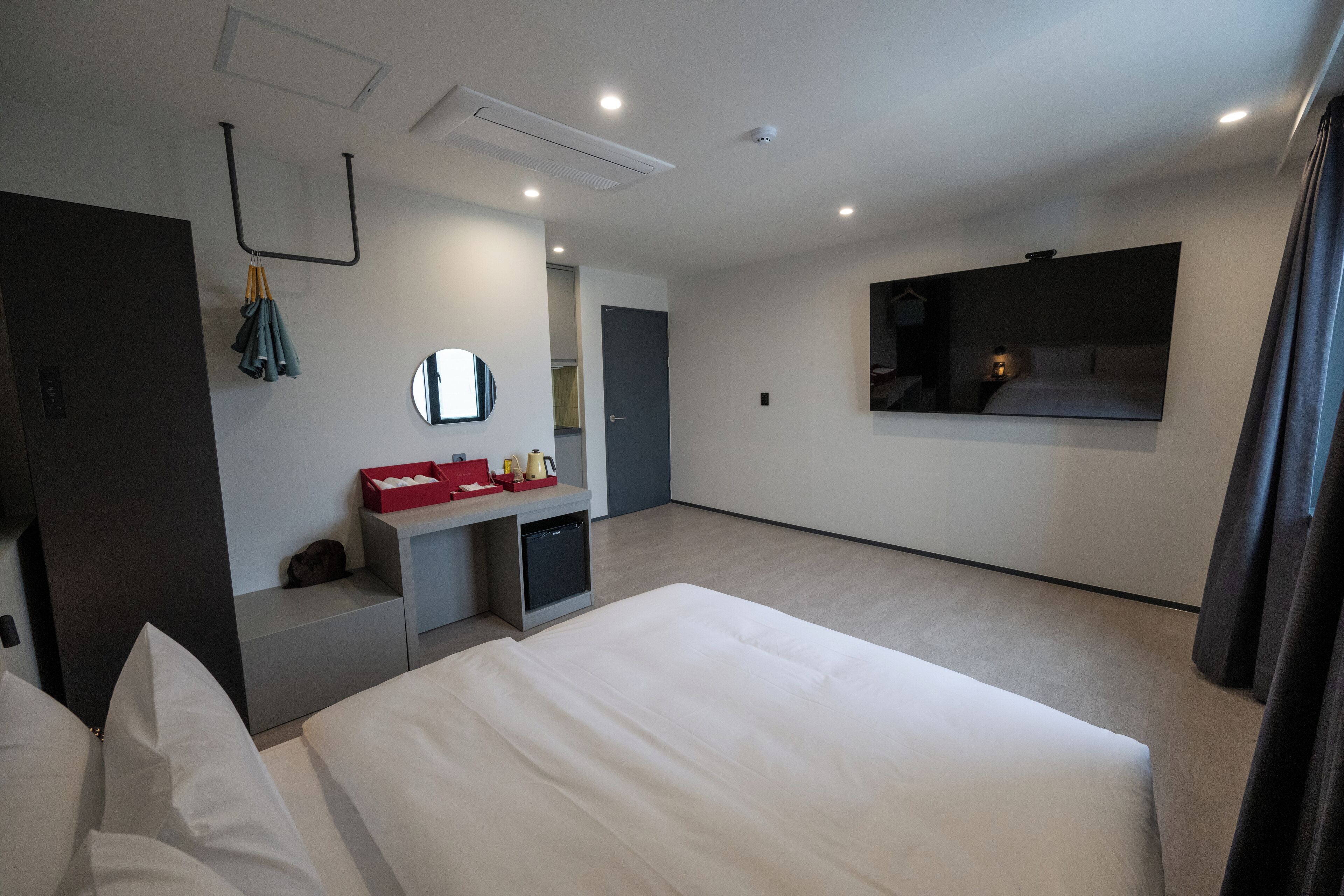 A modern hotel room with a large bed, a small desk with a mirror, and a TV mounted on the wall.