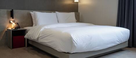 Una habitación de hotel moderna con una cama grande, una mesita de noche con lámpara y un aplique de pared.