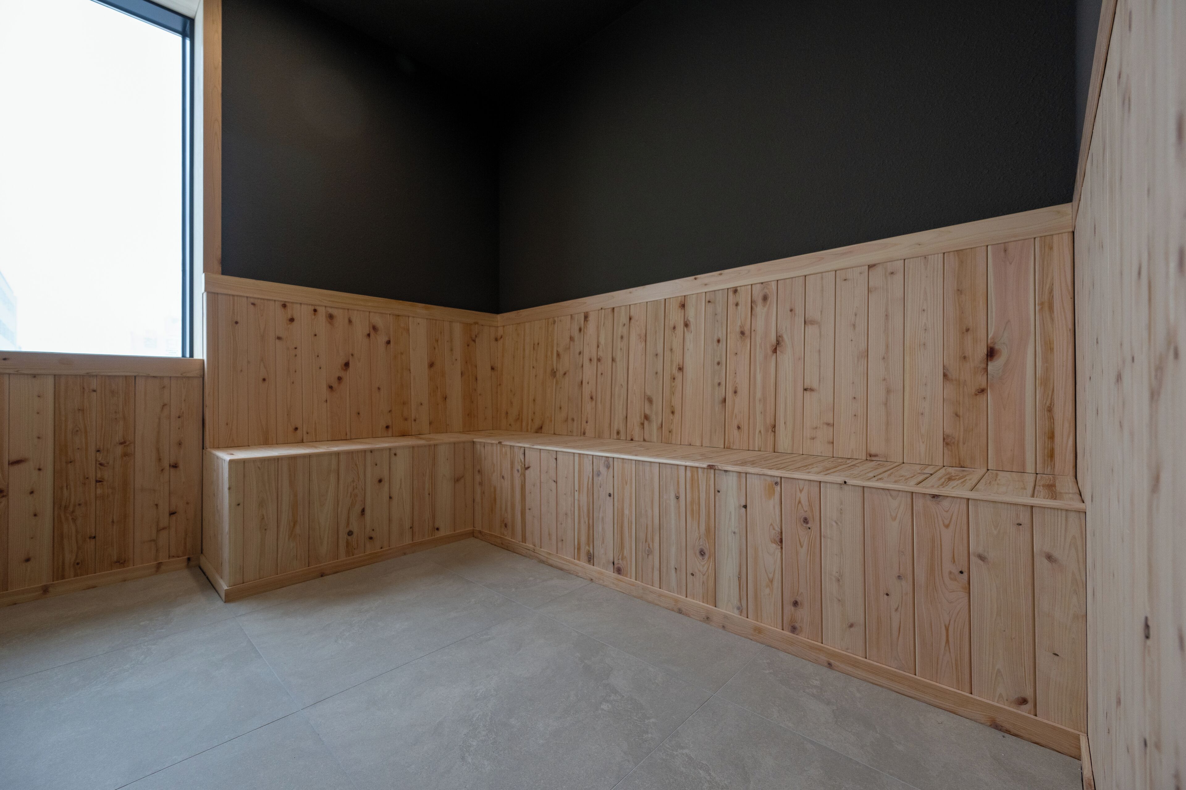 Une pièce d’angle avec des lambris en bois, un plafond sombre et une grande fenêtre.