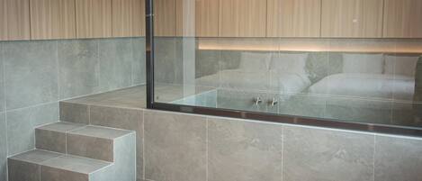 Un baño moderno con ducha de vidrio, banco integrado y suelo de baldosas de piedra.