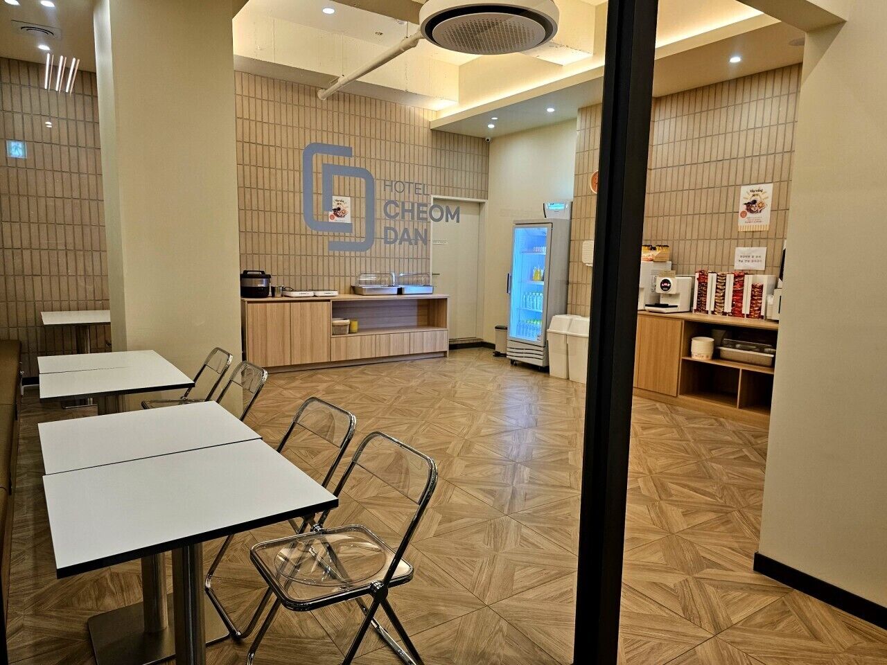 A hotel restaurant with tables and chairs, a counter, and a refrigerator.