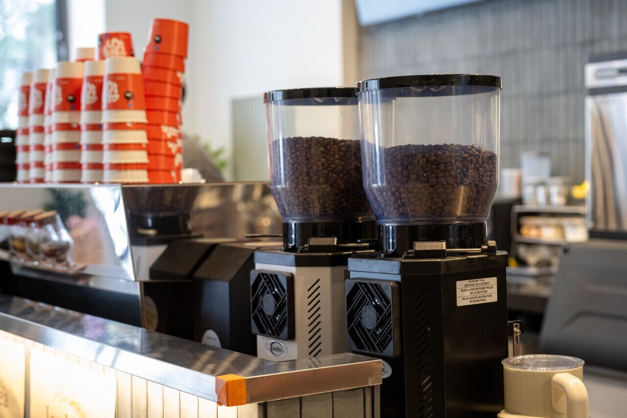 Une machine à café dotée de deux distributeurs de grains de café et d’un mousseur à lait, posée sur un comptoir.